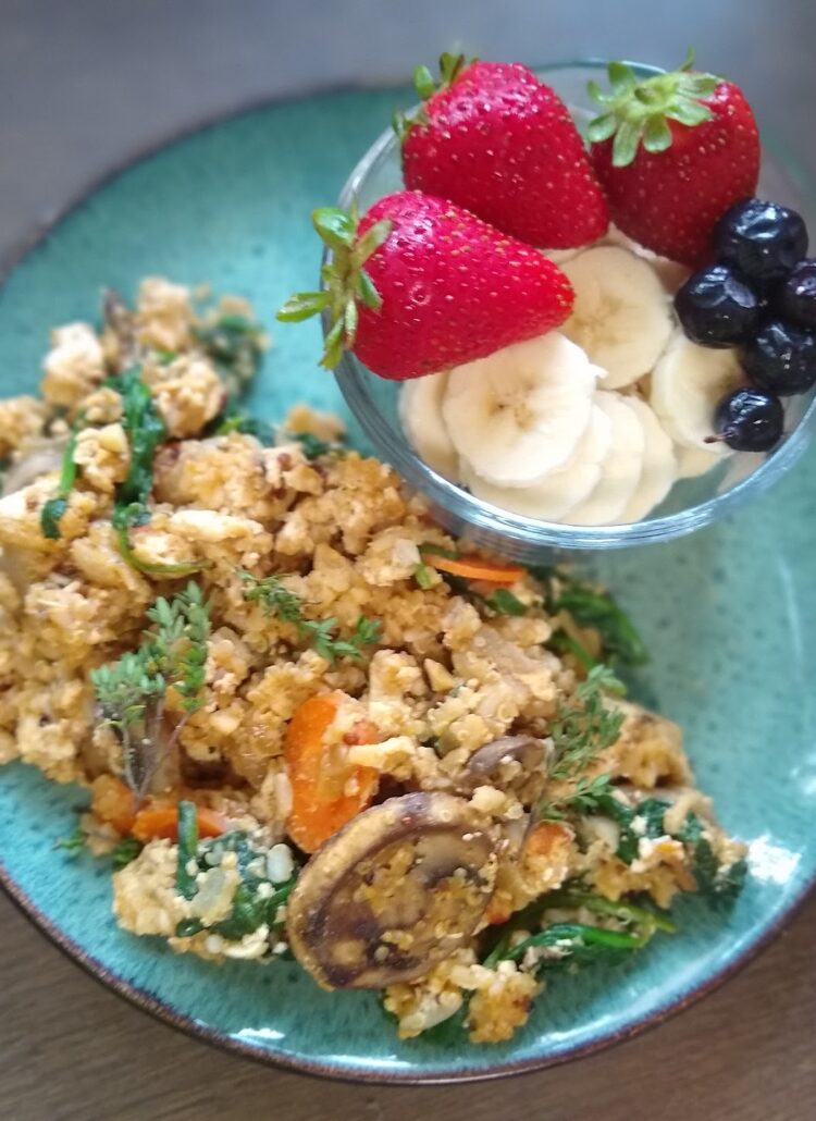 Tofu, brown rice, quinoa, thyme sprigs, mushrooms and a side of strawberries, blueberries and bananas on a plate