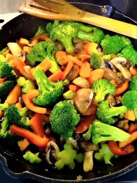 Broccoli, bell peppers, mushrooms and carrots sauteeing without oil in a cast iron pan 